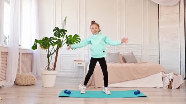 健康的な赤ちゃんの女の子のスポーツマットのスポーツ演習を実行してジャンプを閉じます。健康的なライフスタイル。家庭での子供とスポーツ,スローモーション — ストック動画