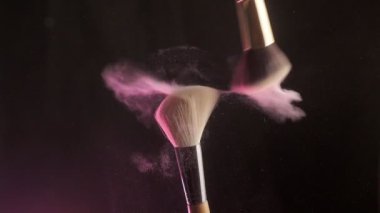 Two makeup brushes with with decorative cosmetics on a dark background, Slow motion