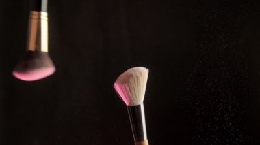 Pembe toz siyah arka planda iki yakın plan makyaj fırçası. Yavaş çekim