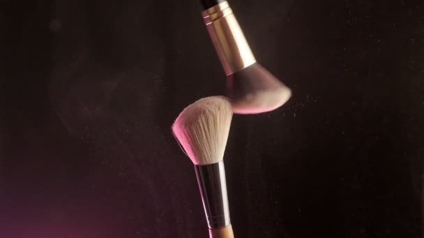 Make-up borstels raken elkaar op donkere achtergrond en kleine deeltjes van cosmetica, slow motion — Stockvideo