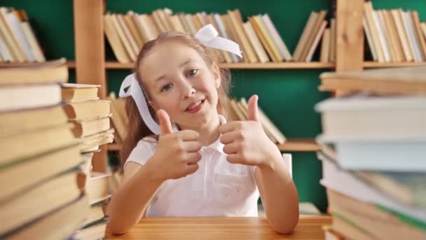 Sorriso feliz menina adolescente 6-10 anos com o polegar para cima olhando para a câmera na biblioteca, Escola primária de educação, câmera lenta — Vídeo de Stock
