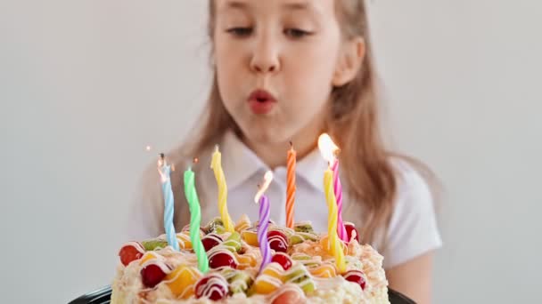 Κοντινό πλάνο του χαριτωμένο κορίτσι σβήνει κεριά σε μια τούρτα στα γενέθλια. Το χαρούμενο παιδί κοιτάζει μια τούρτα με κεριά. Κορίτσι γιορτάζει τα γενέθλια. Ευτυχία έννοια, αργή κίνηση — Αρχείο Βίντεο