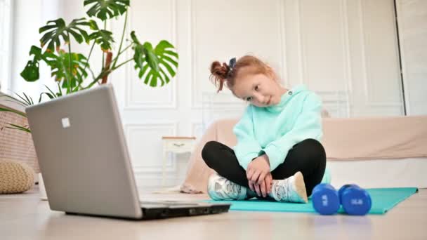 Ragazza adolescente pensierosa seduta davanti al computer portatile che fa esercizi sportivi. Bambini seduti sul pavimento di fronte a un computer portatile che fanno sport. Adolescenti e sport — Video Stock