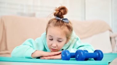Bir ilkokul kızı beden eğitiminden sıkılır. Liseli kız, spor malzemelerine üzülerek bakar ve paspasın üzerine uzanır..