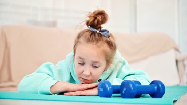 Ein Grundschulmädchen langweilt sich beim Sportunterricht. Die Schülerin blickt traurig auf das Sportgerät und liegt auf der Matte. — Stockvideo