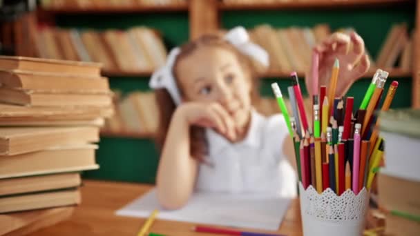 Різнокольорові олівці. На передньому плані олівці на фоні дівчини і бібліотеки — стокове відео