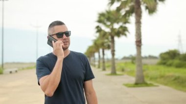 Telefonda bir adam gezinti güvertesinde palmiye ağaçlarıyla yürüyor. Palmiye ağaçlarının arka planındaki tatilden yavaş çekimde çağrı