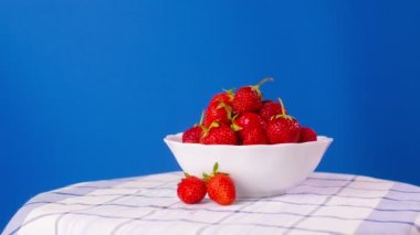A plate with ripe strawberries rotates on a blue background.