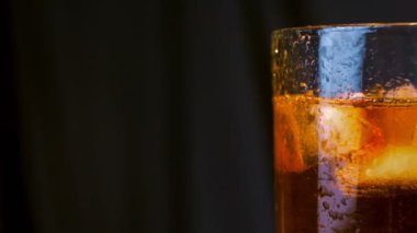 Luxury whiskey. Ice cubes fall with splashes into a glass with golden whisky on the black background. Scotch in tumbler. Bourbon in highball