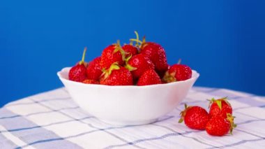 Rotation of juicy strawberries on blue background. Side view, extreme close up