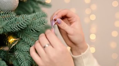 Noel ağacı süslemek. Kadın elleri parlak renkli çelenklerin arka planında kırmızı süslemelerle Noel ağacını süslüyor..
