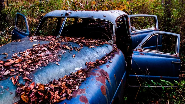 Ein verrostetes, verlassenes, mit Laub bedecktes Auto, das im — Stockfoto