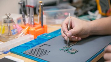 Telefon tamiri kavramı. Çıplak elle tutulan cımbızlar. Devre kartının küçük bir parçasını dikkatlice ve tam olarak ahşap masanın üzerinde kavrıyor..