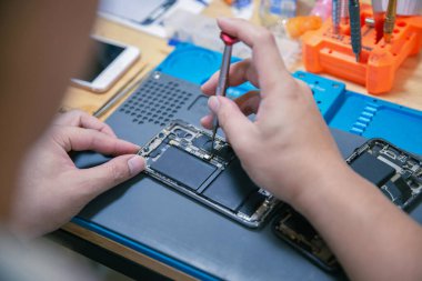 Telefon tamir konsepti. Genç bir elektrik teknisyeni, elektronik bir cihazın parçalarını tornavida kullanarak takıyor..