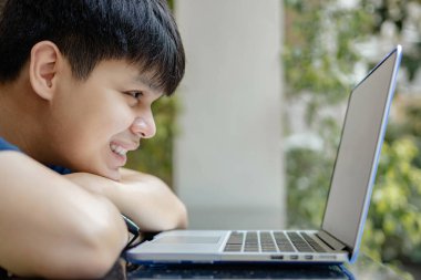 Çevrimiçi konsept üzerinde çalışan genç çocuk çenesini kollarına dayayıp dizüstü bilgisayara bakıyor, işine devam etmek için hiçbir fikri yok, bu da onu şu anda çalışmaktan bezdiriyor..