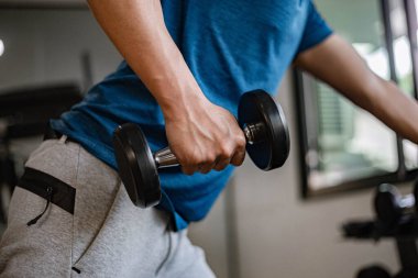Spor salonu konsepti. Genç bir yetişkin, kaslı güçlü kolunu kullanarak spor salonunda bir dambılı yukarı bir aşağı kaldırıyor..