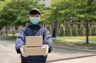 Paket teslimatı konsepti. Genç gönderici iki kutu paket kaldırıyor ve bu iki paketi atmak için dar bir caddenin ortasında duruyor..