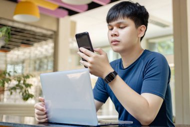 Çevrimiçi araştırma konsepti üzerinde çalışan koyu mavi gömlekli ve siyah saatli genç adam, arkadaşlarını aramak için akıllı telefonunu kullanıyor çünkü şu anda online toplantıda görünmüyorlar..