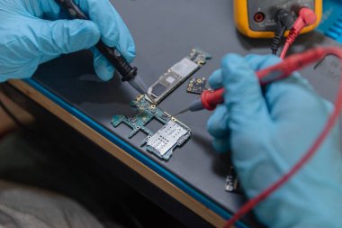 Telefon tamir konsepti. Genç bir elektrik teknisyeni bir elektronik cihazın akımını ölçmek için bir ammetre kullanıyor..