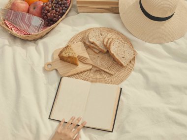 Piknik konsepti. Beyaz kumaş üzerinde bir sürü şey var. Ekmek, meyve, bir şişe su, şapka ve defter gibi..