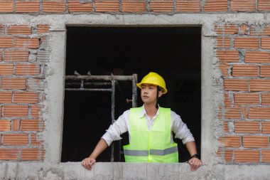 Mühendis konsepti. Genç inşaatçı ellerini pencerenin kenarına koyar ve gözlerini önündeki manzaraya koyar..