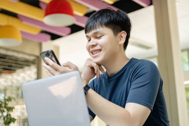 Çevrimiçi araştırma konsepti üzerinde çalışan koyu mavi tişörtlü ve siyah saatli genç adam, arkadaşlarını aramak için akıllı telefonunu kullanıyor çünkü şu anda online toplantıda görünmüyorlar..