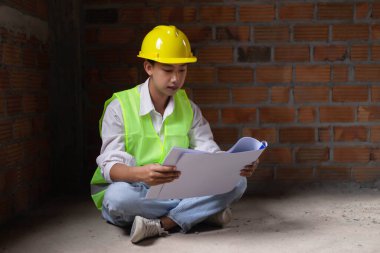 Mühendis konsepti. Erkek müteahhit yere oturup bugünkü çalışma planını ciddi bir suratla okuyor..