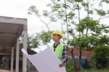 Mühendis konsepti Sert sarı şapka giyen, koyu renkli ekose bluz giyen ve inşaat binasına bakan inşaat manipülatörü.