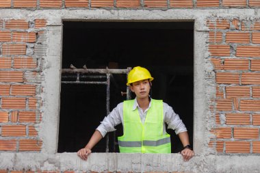 Mühendis konsepti. Genç inşaatçı ellerini pencerenin kenarına koyar ve gözlerini önündeki manzaraya koyar..