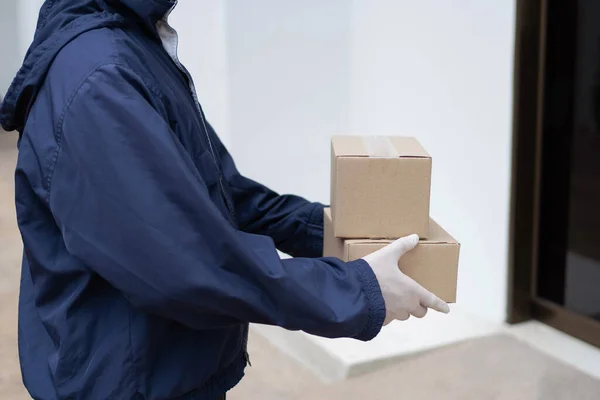 小包配達コンセプトは 白いゴム手袋とライトウェイトダークブルーのコートの郵便配達人は 建物の前で彼のクライアントに小さな小包を渡すのを待っています — ストック写真