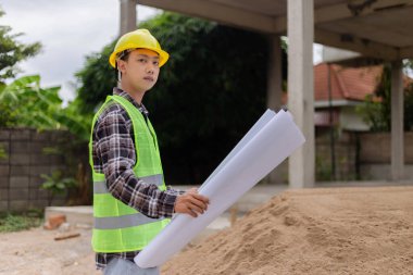Mühendis konsepti Sert sarı şapka giyen, koyu renkli ekose bluz giyen ve inşaat binasına bakan inşaat manipülatörü.