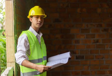 Mühendis konsepti Erkek baş müteahhit kendini pencere çerçevesine yaslıyor, planını tutuyor ve inşaatın yapısına bakıyor..