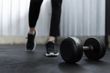 Egzersiz konsepti siyah lastik kaplı yuvarlak dambıl spor salonunda siyah spor ayakkabıları giyen kişinin önünde duruyordu..