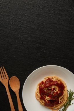 makarna konsepti kırmızı soslu haşlanmış uzun ince makarna ahşap kaşık ve çatalla birlikte siyah masada servis ediliyor..