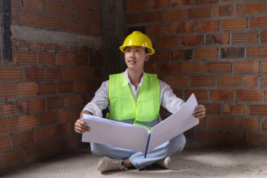 Mühendis konsepti. Erkek müteahhit yere oturup bugünkü çalışma planını ciddi bir suratla okuyor..