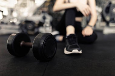 Egzersiz konsepti. Koyu renk elbiseli kadın halı döşemesinde dinleniyor. Yanında duran halterde oynadıktan sonra..