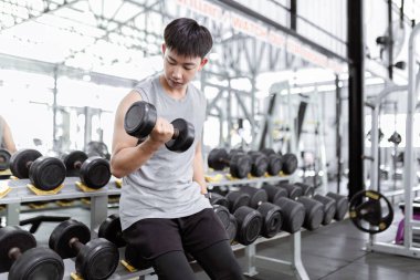 Spor konsepti. Gri spor bluzlu, siyah pantolonlu kaslı adam. Sağ kolunda konsantrasyon kıvrımı yaparak halterle çalışan siyah bir akıllı adam..