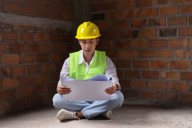 Mühendis konsepti. Erkek müteahhit yere oturup bugünkü çalışma planını ciddi bir suratla okuyor..