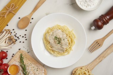 makarna konsepti kaynamış uzun ince makarna beyaz fayans masasında servis ediliyor ahşap kaşık ve çatal, küçük kırmızı domates ve diğer malzemelerle birlikte..