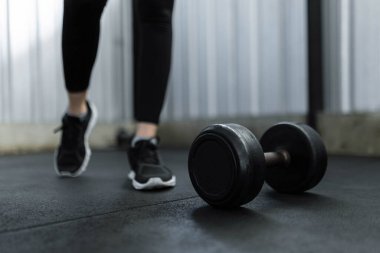 Egzersiz konsepti siyah lastik kaplı yuvarlak dambıl spor salonunda siyah spor ayakkabıları giyen kişinin önünde duruyordu..