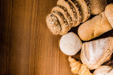 Ekmek kavramı. Tohumlu, çörekli, kruvasanlı ve somun ekmekli birkaç dilim koyu kahverengi ekmek ahşap arka planda bir araya getirildi..