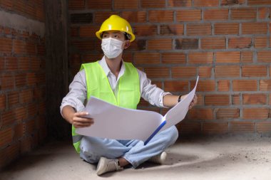 Mühendis konsepti. Erkek inşaatçı, binanın zeminine tüneyen, bina diyagramını açan ve gözlerini binanın duvarına dikmiş..