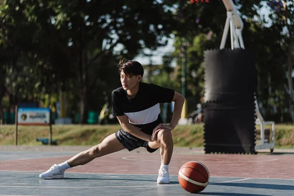 在篮球场打篮球之前 身穿黑衣的亚洲男孩伸腿打篮球 — 图库照片