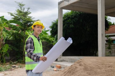 Mühendis konsepti Sert sarı şapka giyen, koyu renkli ekose bluz giyen ve inşaat binasına bakan inşaat manipülatörü.