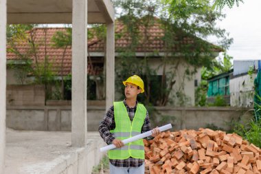 Mühendis konsepti açık yeşil gömlekli genç mühendis ve binanın ikinci katını gösteren sarı kasklı adam..