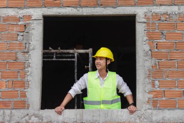 Mühendis konsepti. Genç inşaatçı ellerini pencerenin kenarına koyar ve gözlerini önündeki manzaraya koyar..