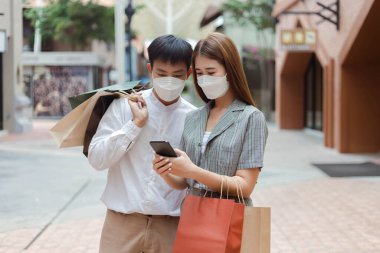 Alışveriş konsepti. Erkek alışveriş torbalarını sırtında tutuyor ve kadın alışveriş torbalarını kolunda taşıyor. Akıllı telefon ekranına bakıyor..