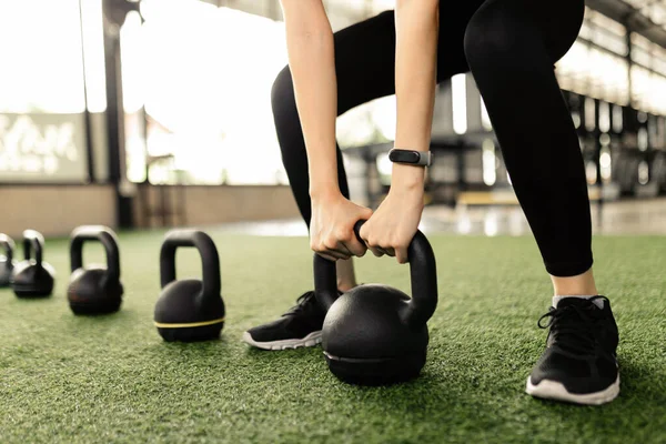 exercise concept The black kettlebells being lined on the green carpet for being done kettlebell swing by someone who wears a grey smartwatch and black pair of shoes.