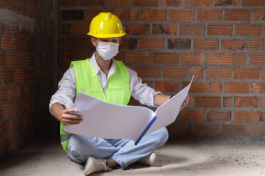 Mühendis konsepti. Erkek inşaatçı, binanın zeminine tüneyen, bina diyagramını açan ve gözlerini binanın duvarına dikmiş..