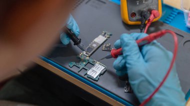 Telefon tamir konsepti. Genç bir elektrik teknisyeni bir elektronik cihazın akımını ölçmek için bir ammetre kullanıyor..